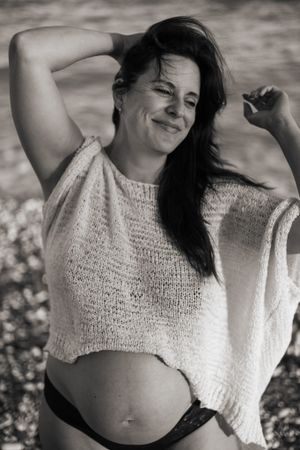 A black and white portrait shows a carefree moment in a loose knit crop top against a blurred outdoor background.