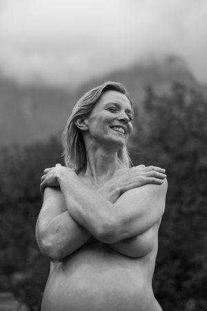 Black and white portrait of a laughing woman in nature with crossed arms.