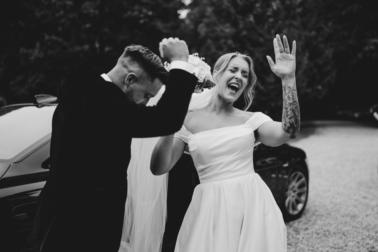 Wedding guests celebrate joyfully outdoors during a summer reception near a white building.