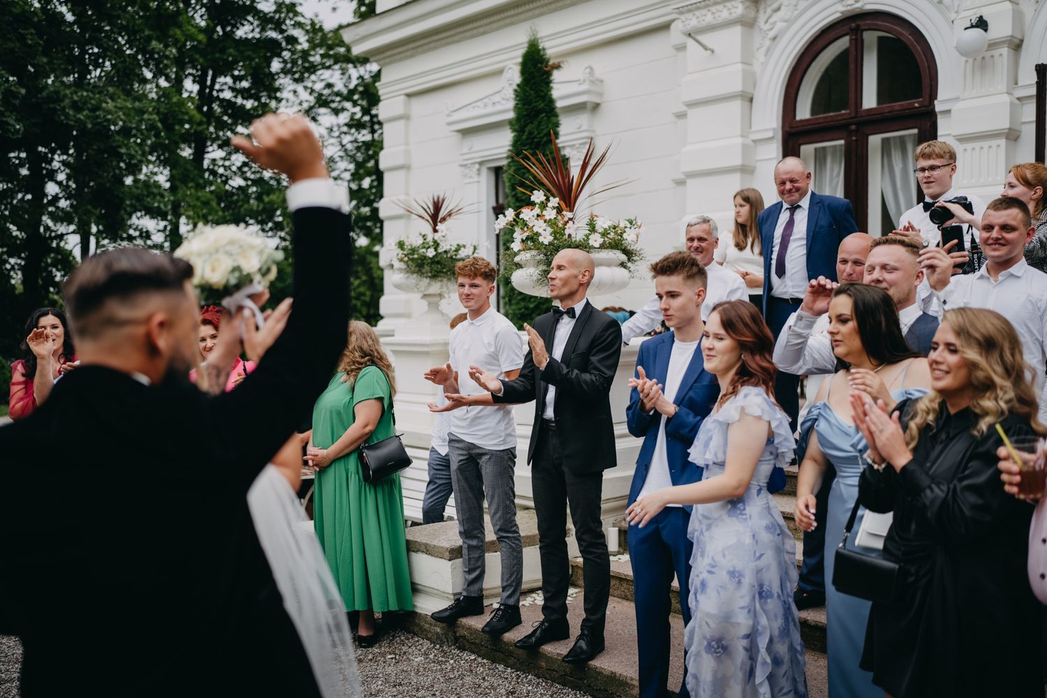 Wedding guests celebrate outdoors at a villa as someone raises a toast.