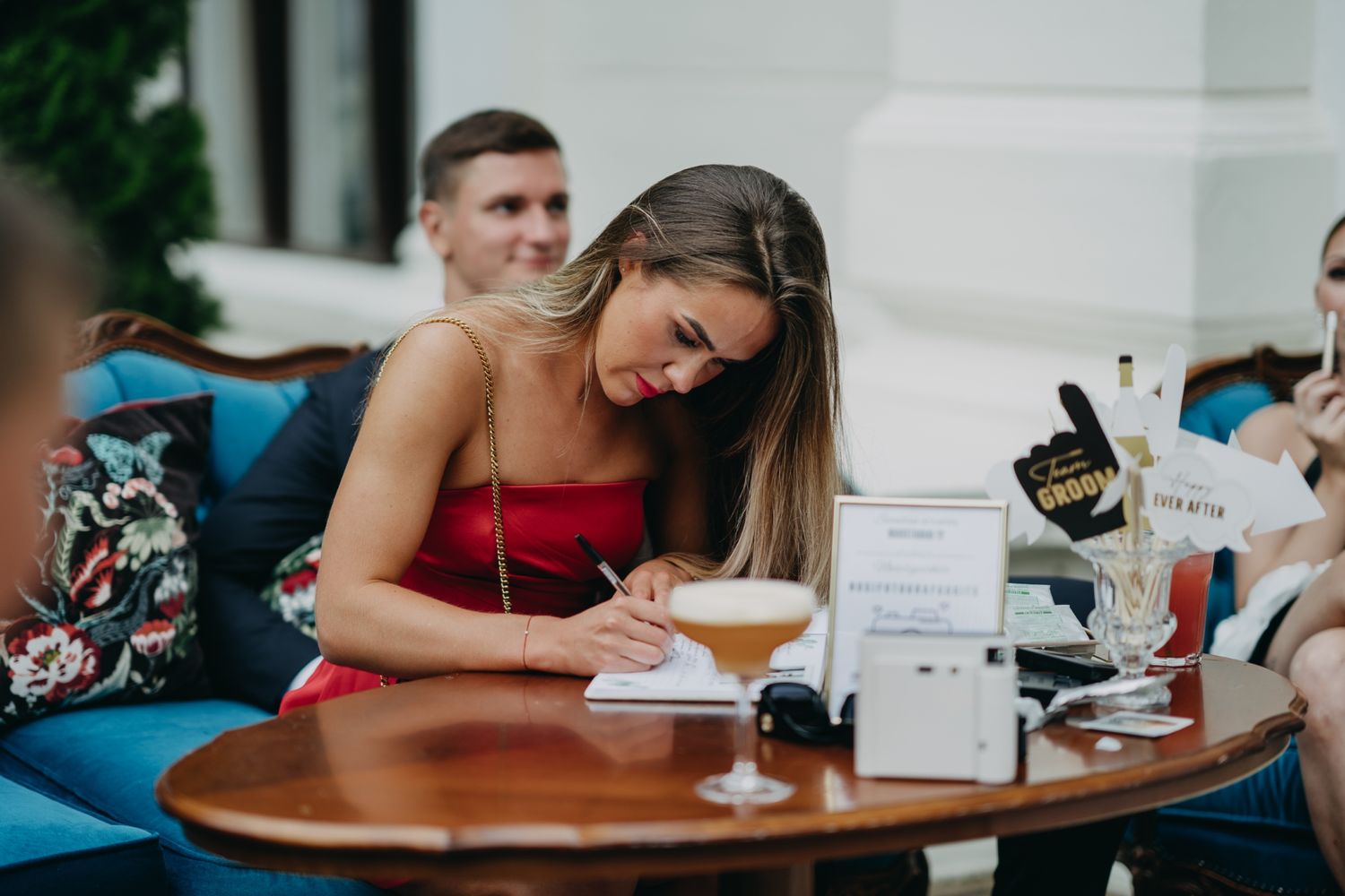 Wedding guests signing guestbook at reception with drinks nearby.