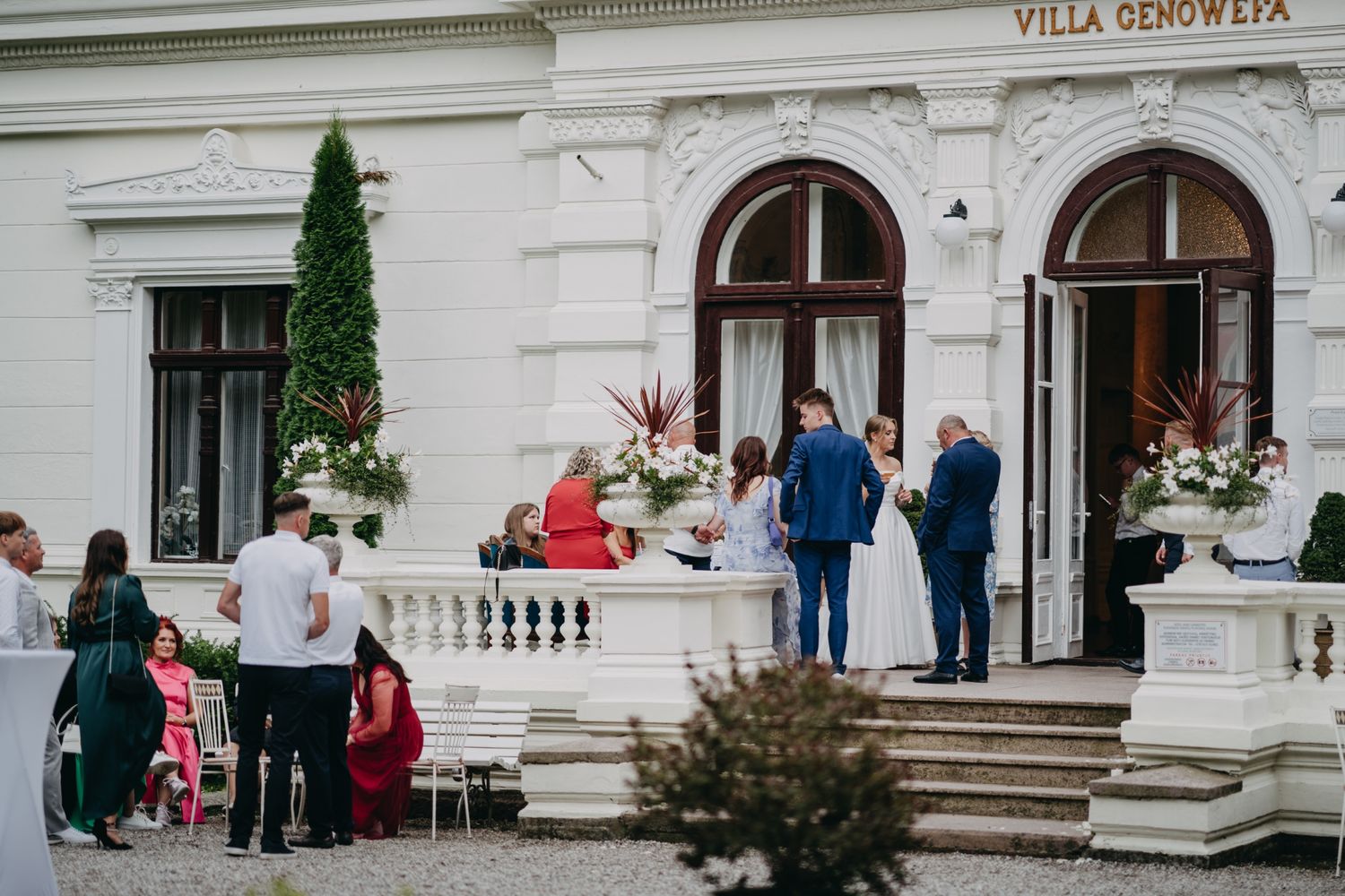 Elegant wedding guests gather outside Villa Geno Eva with its classic white facade and arched doorways.