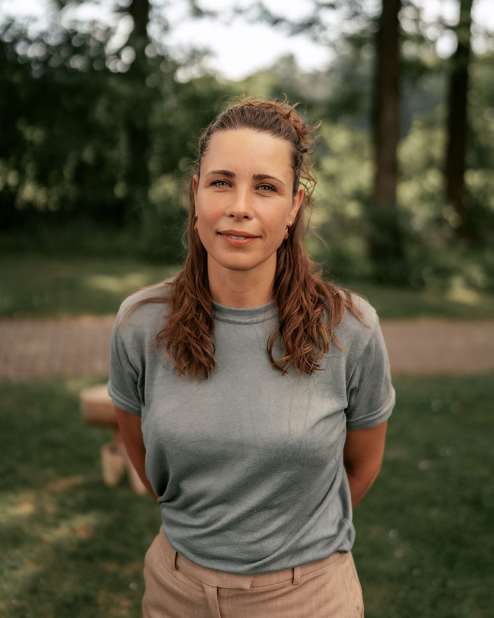Person in grey t-shirt and khaki pants stands outdoors in a park setting with natural lighting.