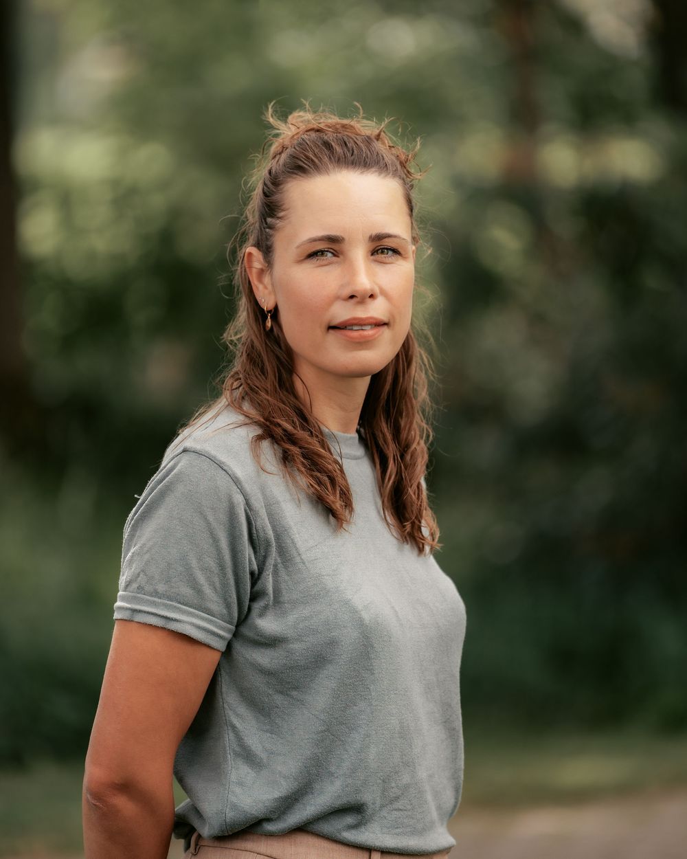 Person wearing a grey t-shirt standing in an outdoor setting with natural bokeh background.