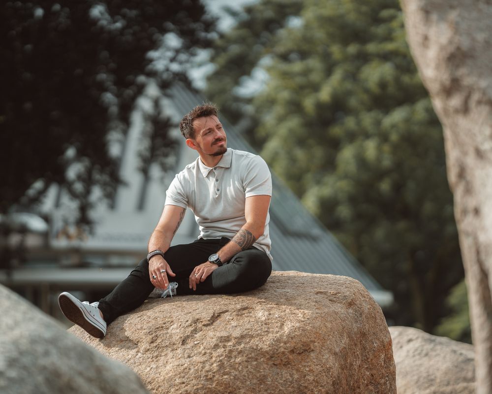 Person in casual wear strikes dynamic poses on large outdoor boulder.