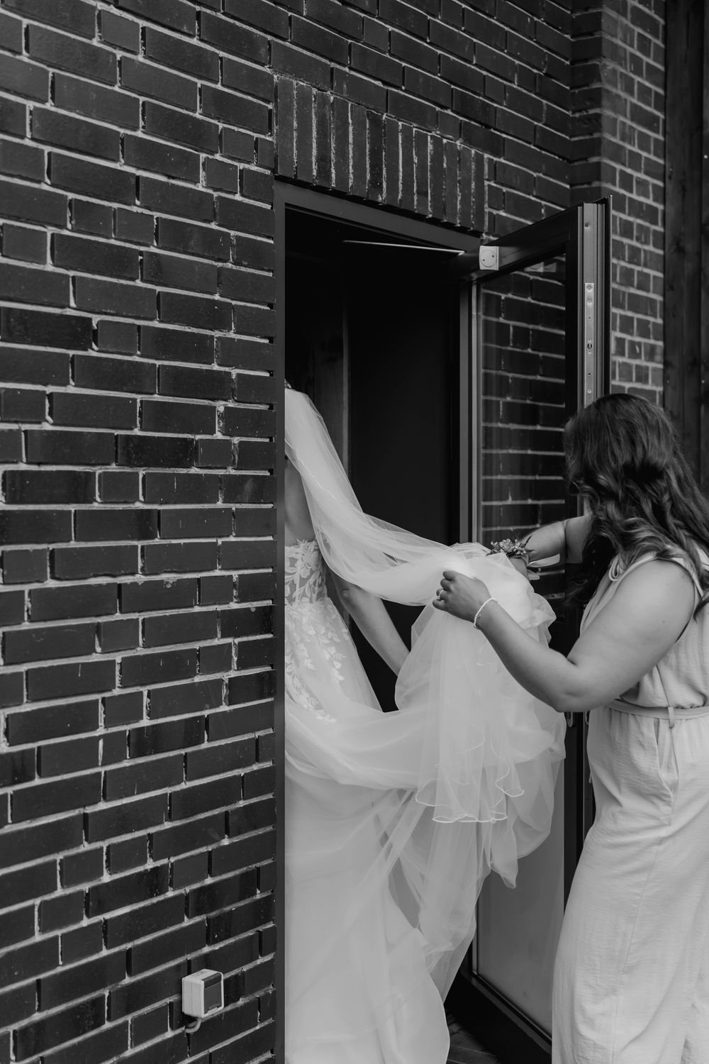 Black and white image of wedding dress being arranged through doorway.