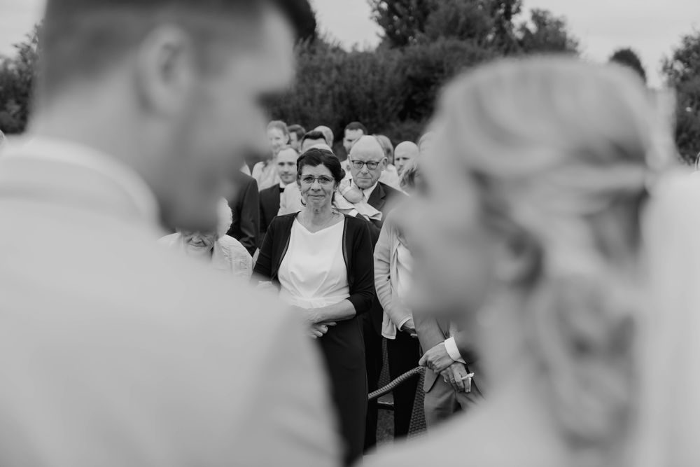 Wedding guests react joyfully during outdoor ceremony on bright sunny day.