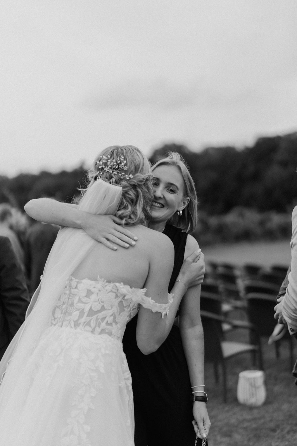 Emotional wedding day embrace between bride in lace gown and guest at outdoor reception.