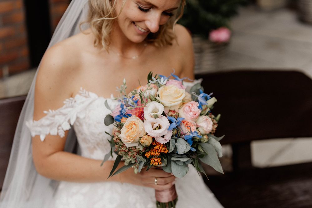 Bride in lace dress holds beautiful pastel bouquet with roses and blue flowers.