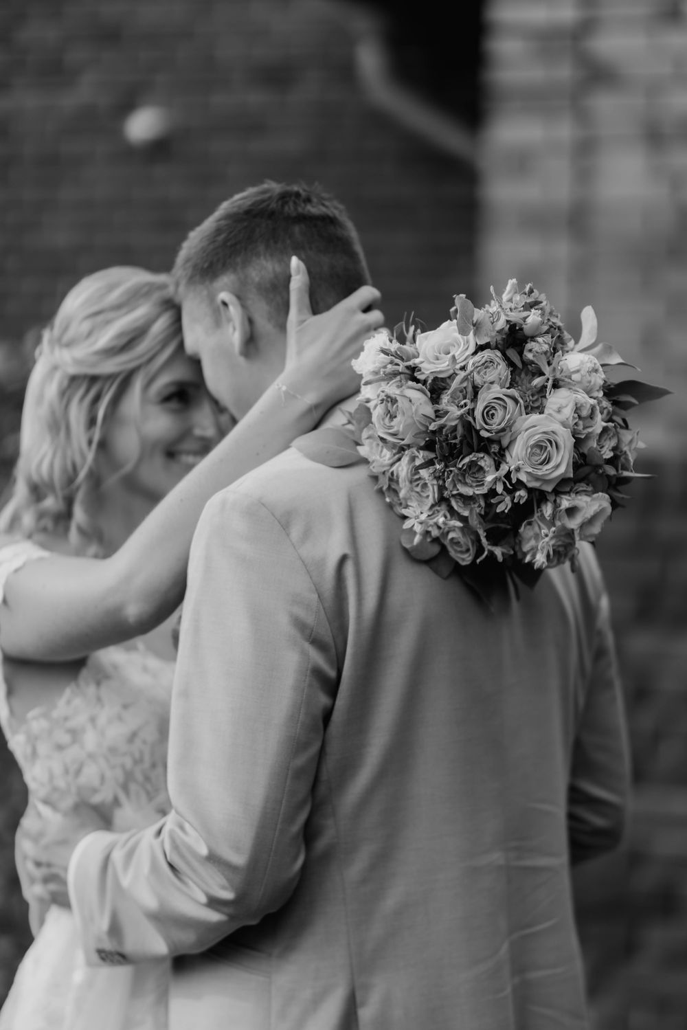 Romantic embrace with wedding bouquet captured in black and white.