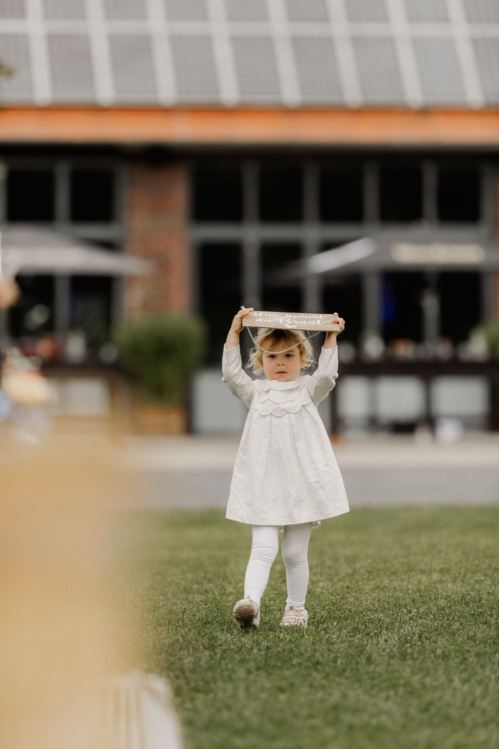 Little girl in white dress playing on lawn during wedding celebration.