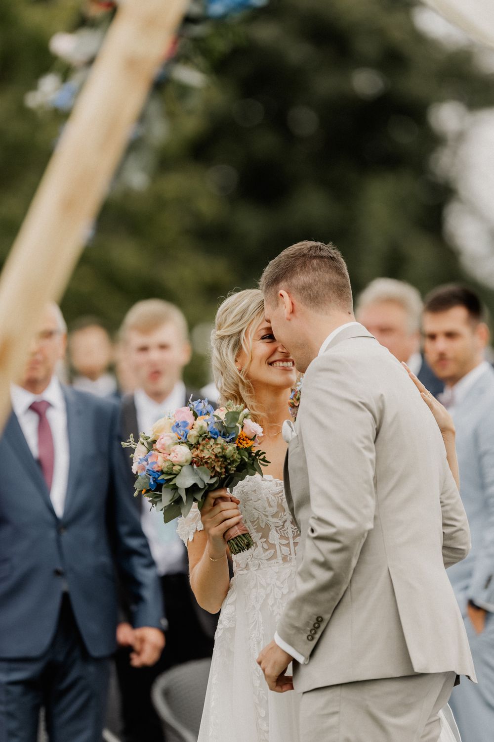 Wedding couple sharing intimate moment at outdoor ceremony with colorful bouquet.