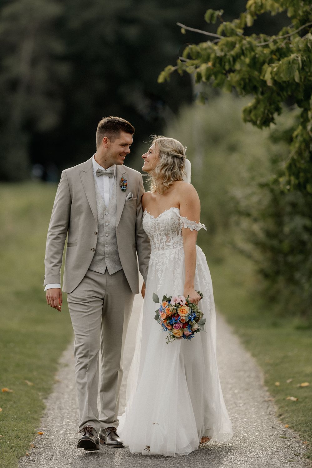 Candid wedding portrait of couple walking along rural path with bouquet.