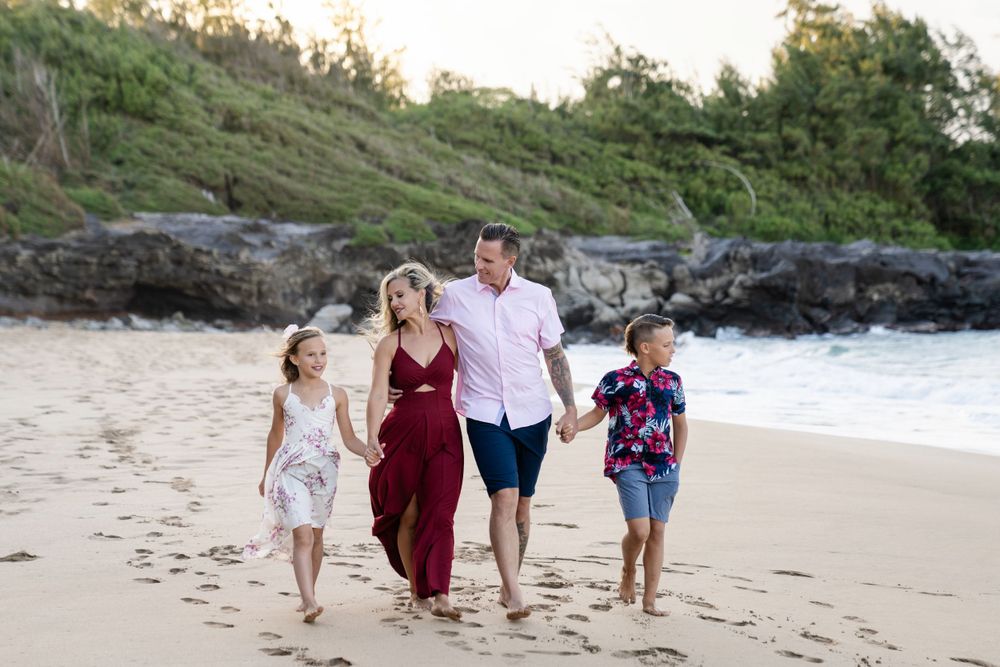 Family leaves footprints in sand while walking together on tropical beach with volcanic rocks.