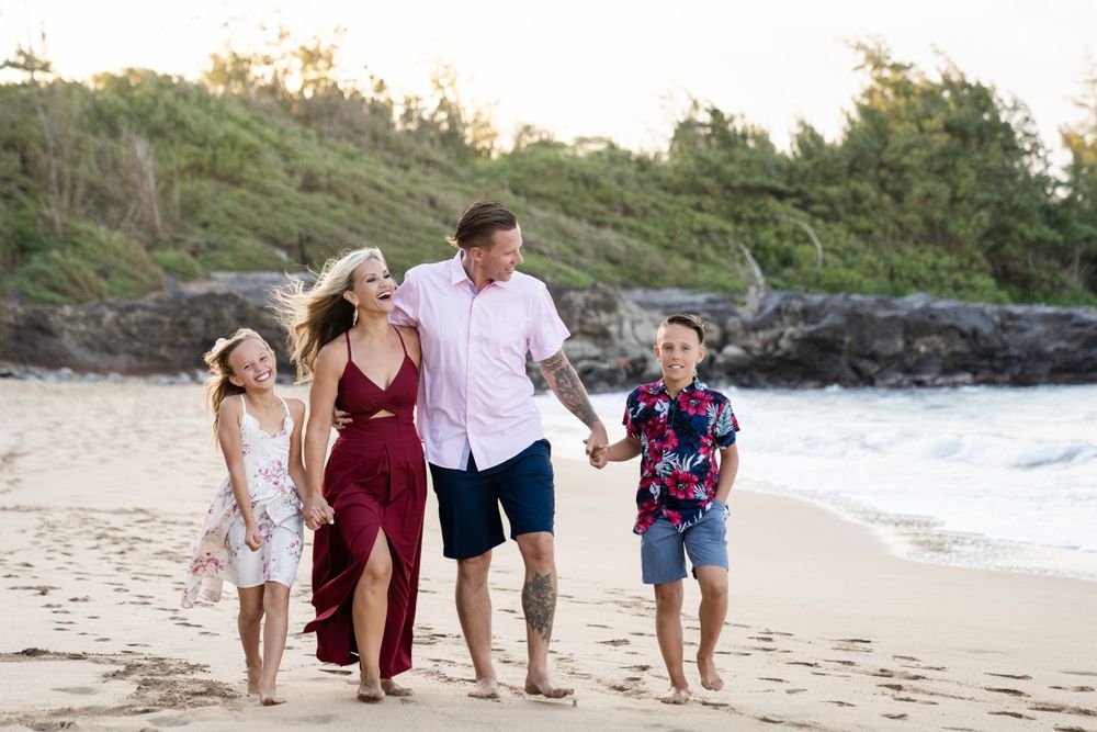 Family walking along ocean shoreline during golden hour with waves and cliffs in view.