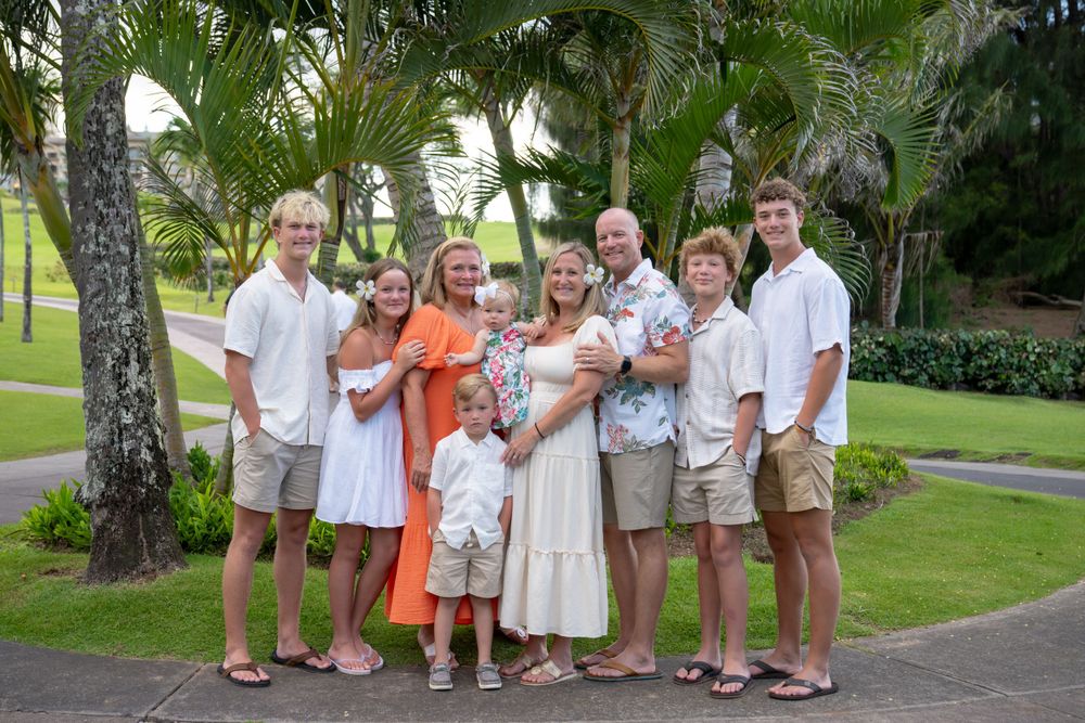 Large family group in coordinated outfits posing together on a tropical palm-lined path.