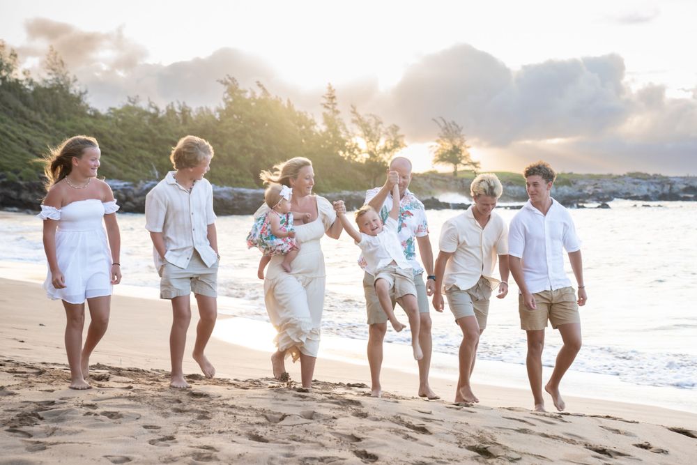 Family walking together on a beach at sunset wearing coordinated white and beige outfits.