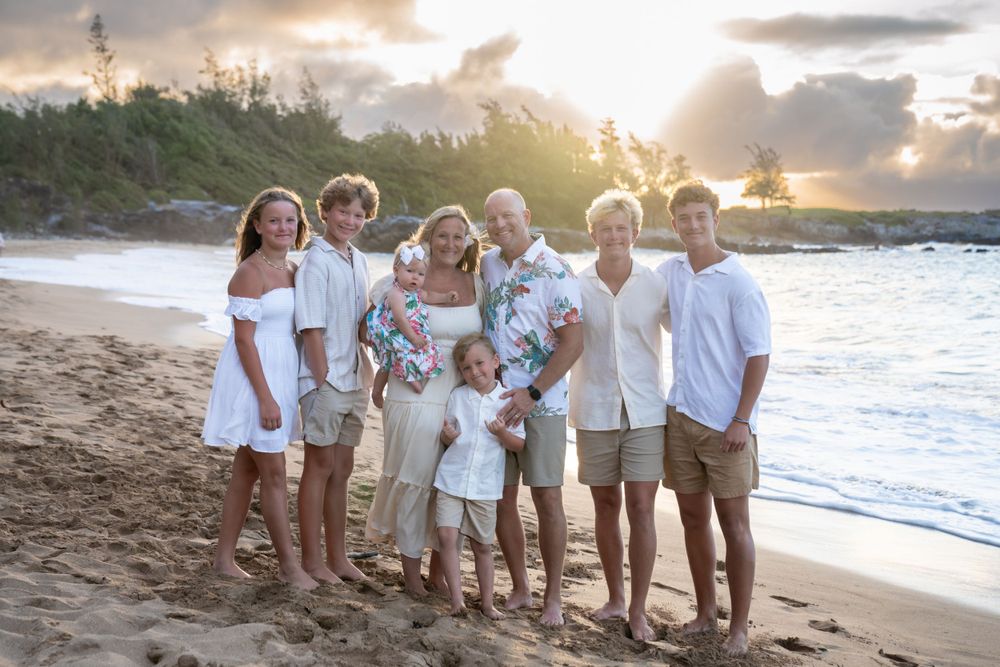 Extended family portrait on a Hawaiian beach at sunset with mountains in background.