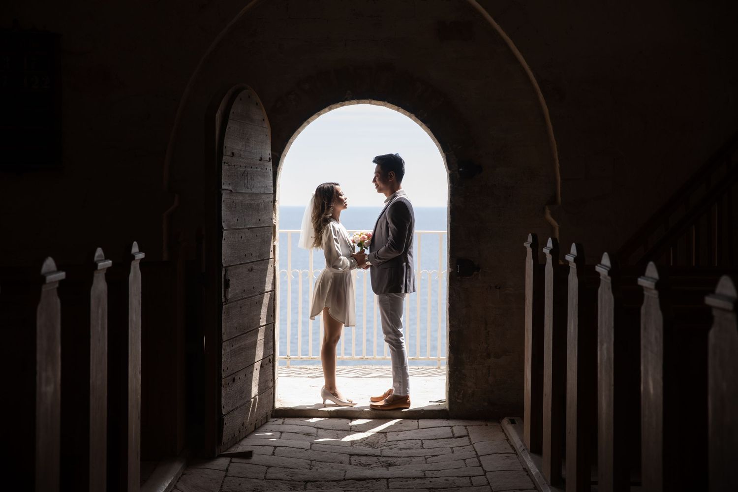 Silhouetted wedding couple standing in an arched stone doorway with bright daylight behind them.