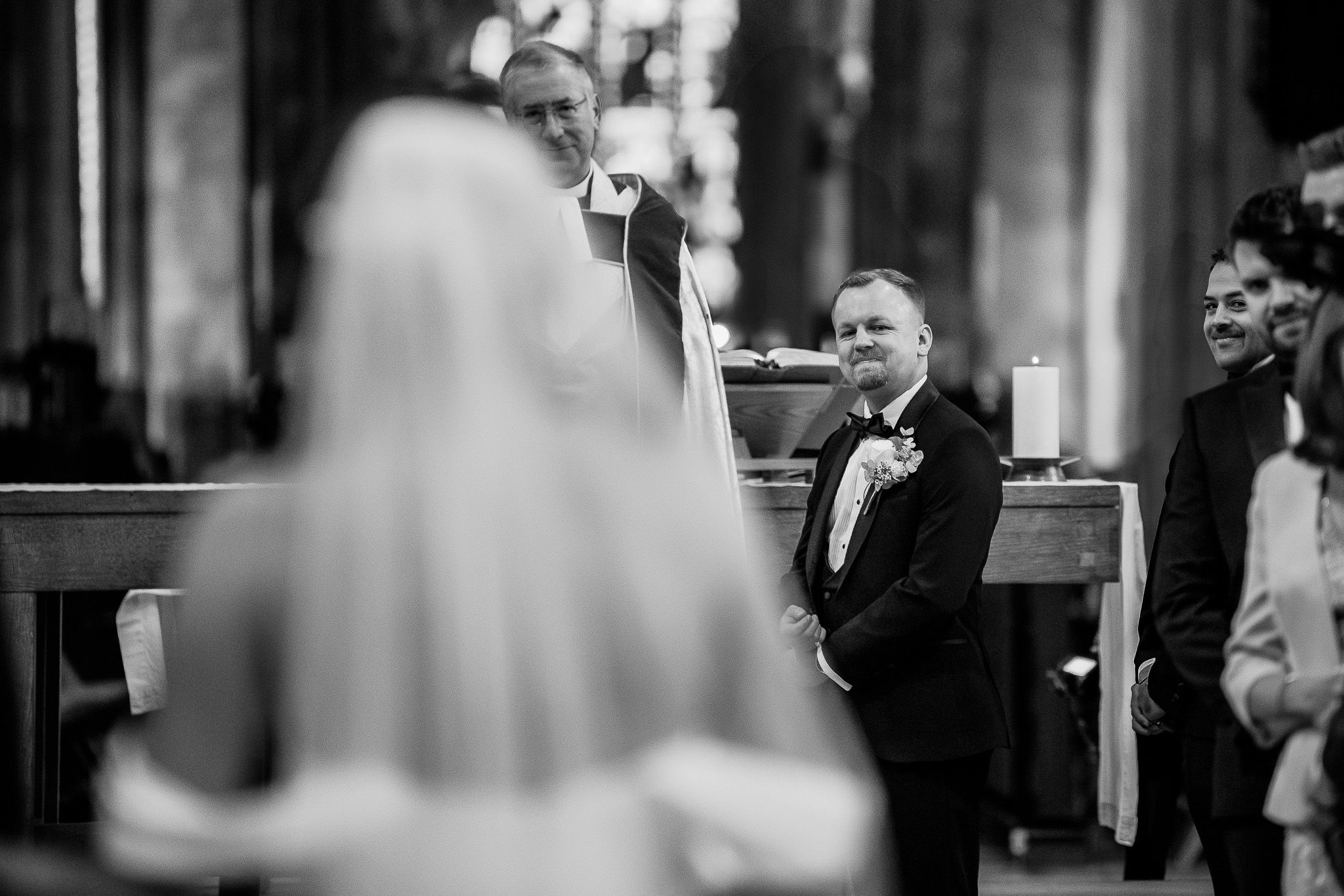 Black and white candid moment during wedding ceremony in traditional church setting.