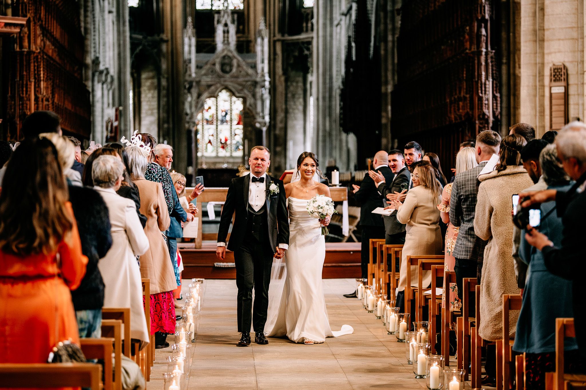 Wedding ceremony taking place in a grand cathedral with guests seated in wooden pews.
