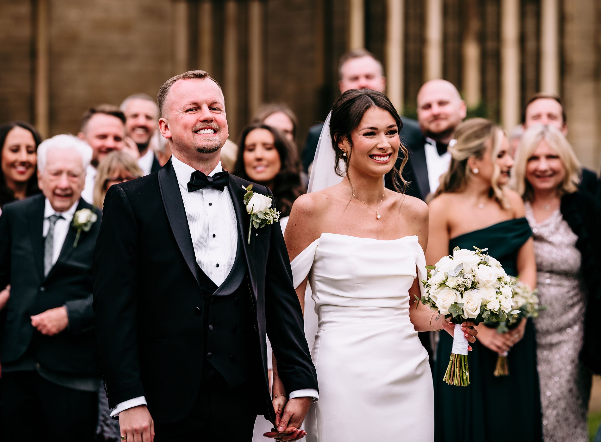 Happy newlyweds walking down church aisle with guests smiling in background.