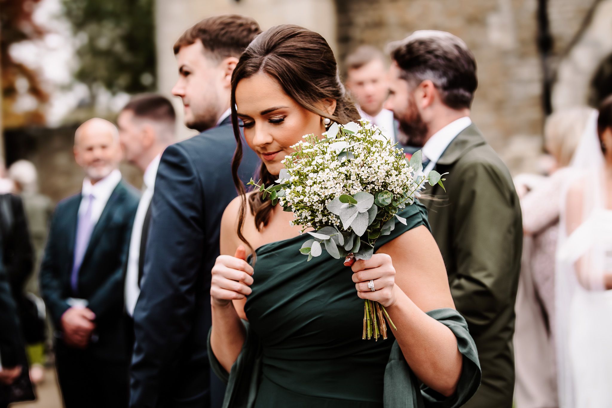 Bridesmaid in dark green dress holding delicate white floral bouquet during ceremony.
