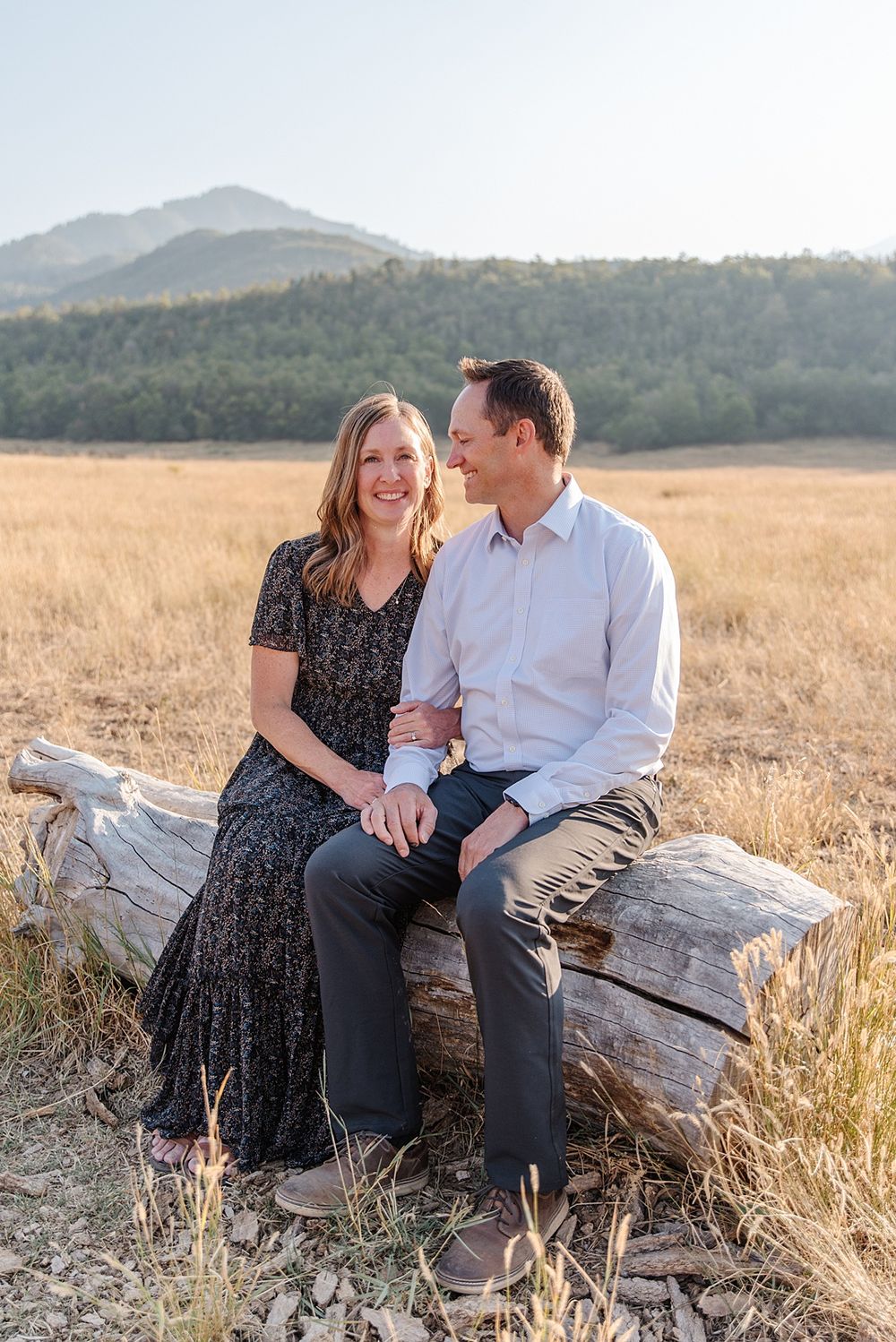 Couple sitting on fallen log in mountain meadow during golden hour.