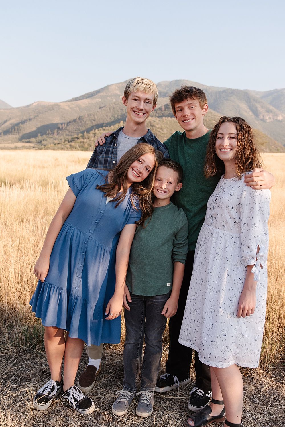 Group portrait of people standing together in mountain field during golden hour.