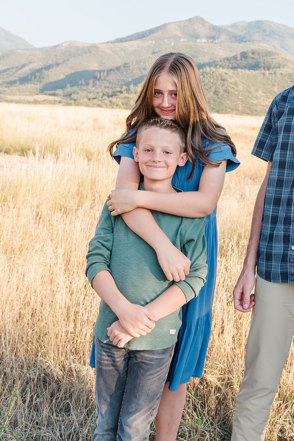 A sweet embrace captured in golden sunlit field with mountains in the background.