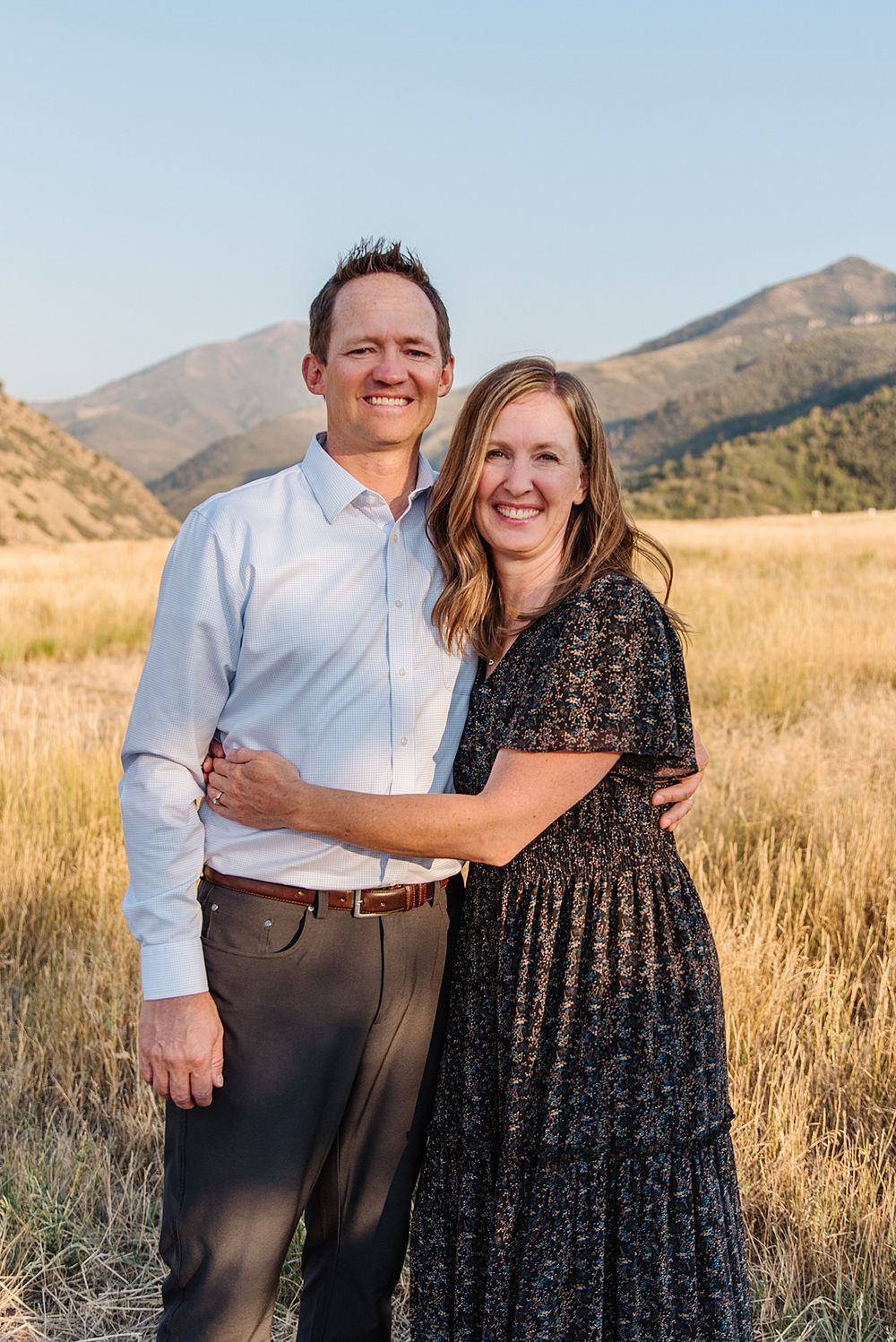 Couple poses together in a serene mountain meadow during golden hour.