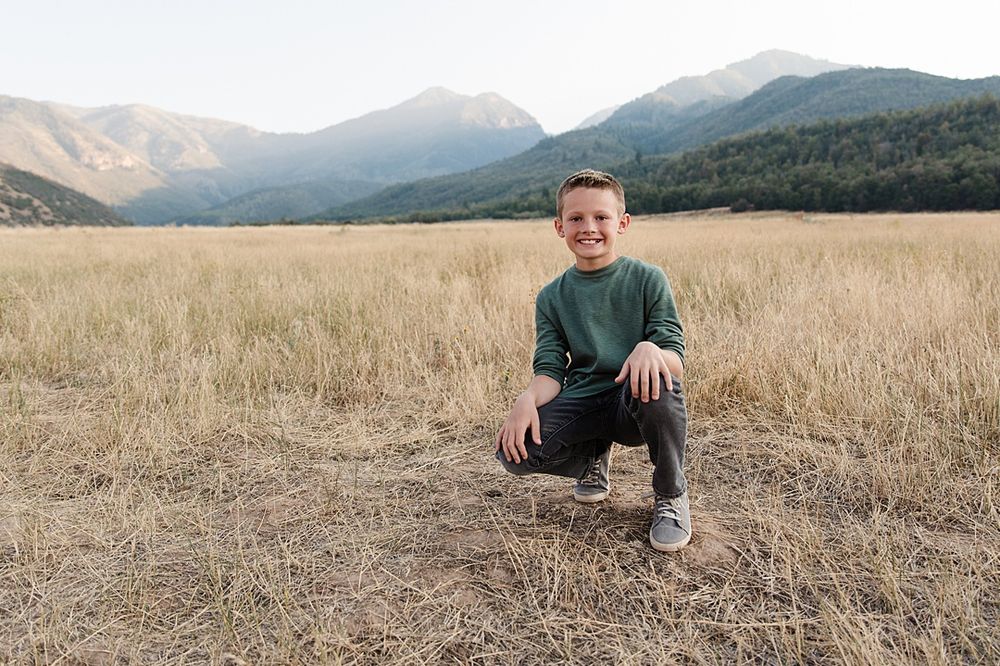 Child kneeling in dry grass field with majestic mountains in the background.