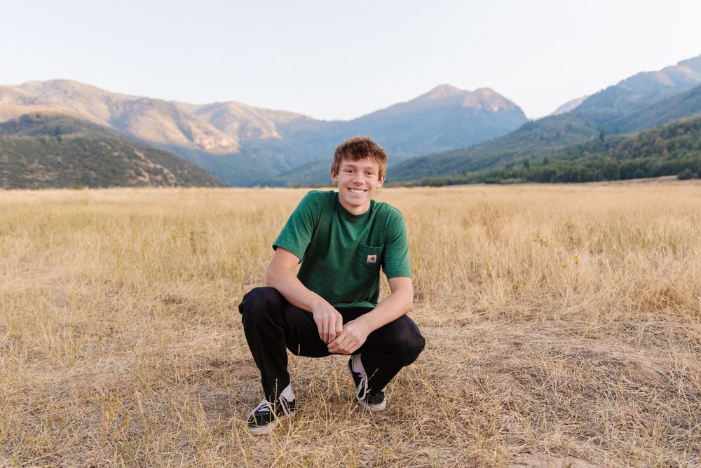Person crouched in a field with mountains in the background during golden hour.