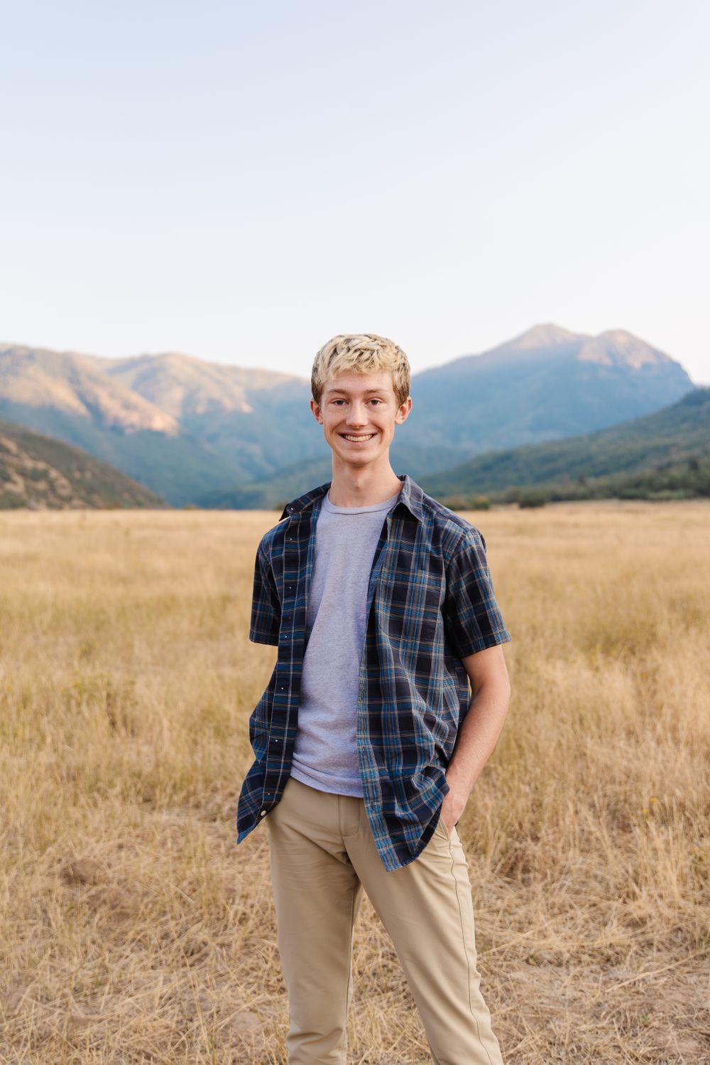 Person standing in casual attire against mountain backdrop in golden field.