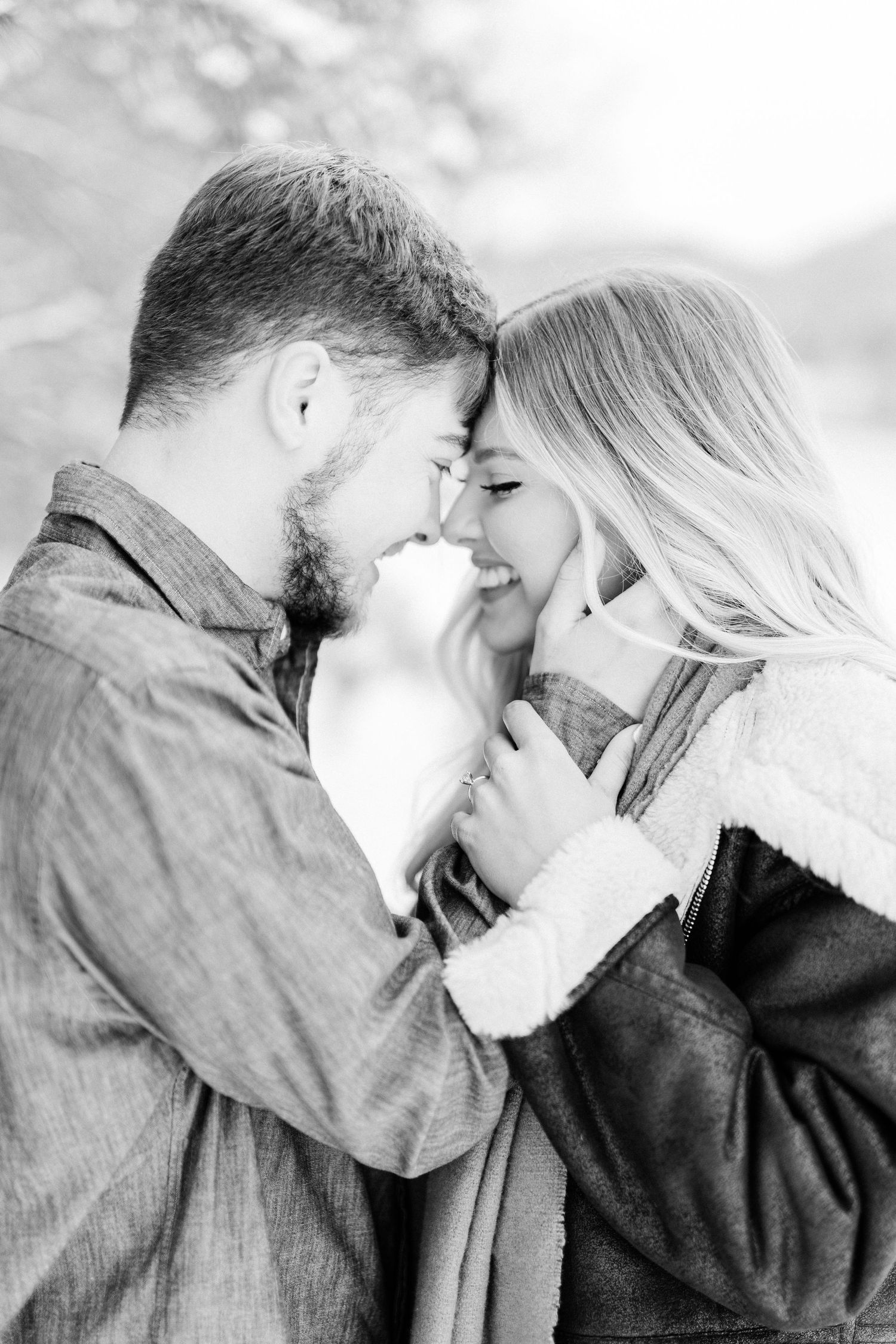 An intimate black and white portrait of a couple sharing a close romantic moment outdoors.