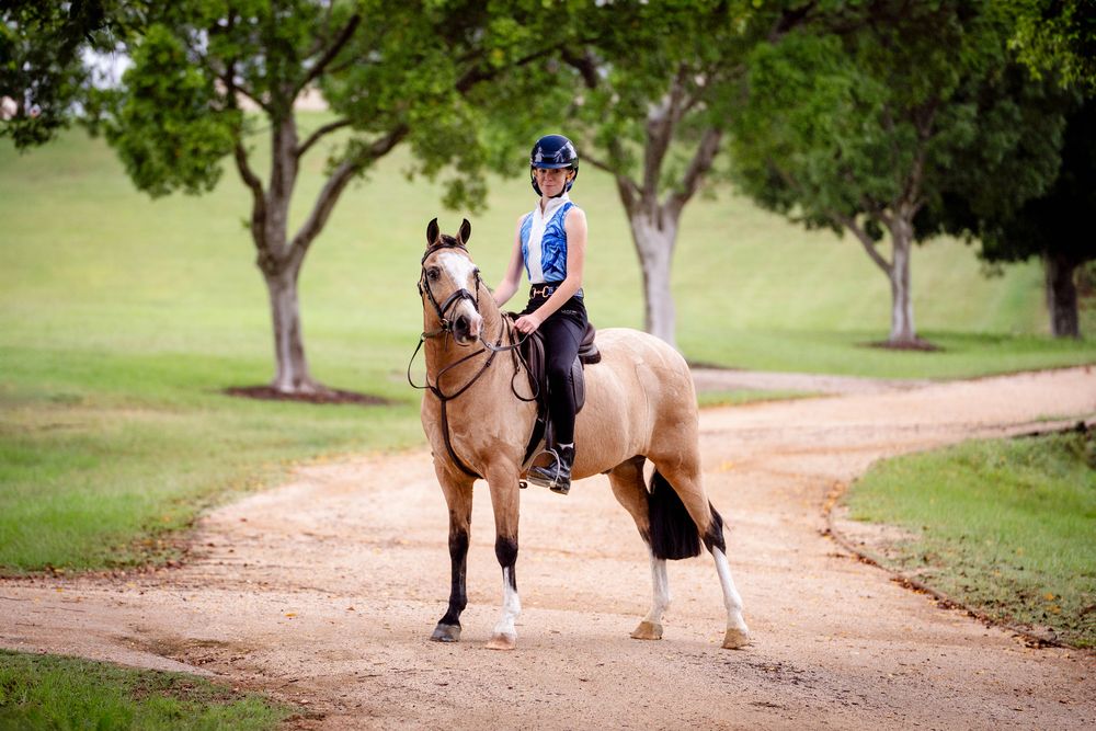 Young rider in helmet atop a buckskin horse on a dirt path surrounded by green trees Sydney International Equestrian Centre photoshoot
