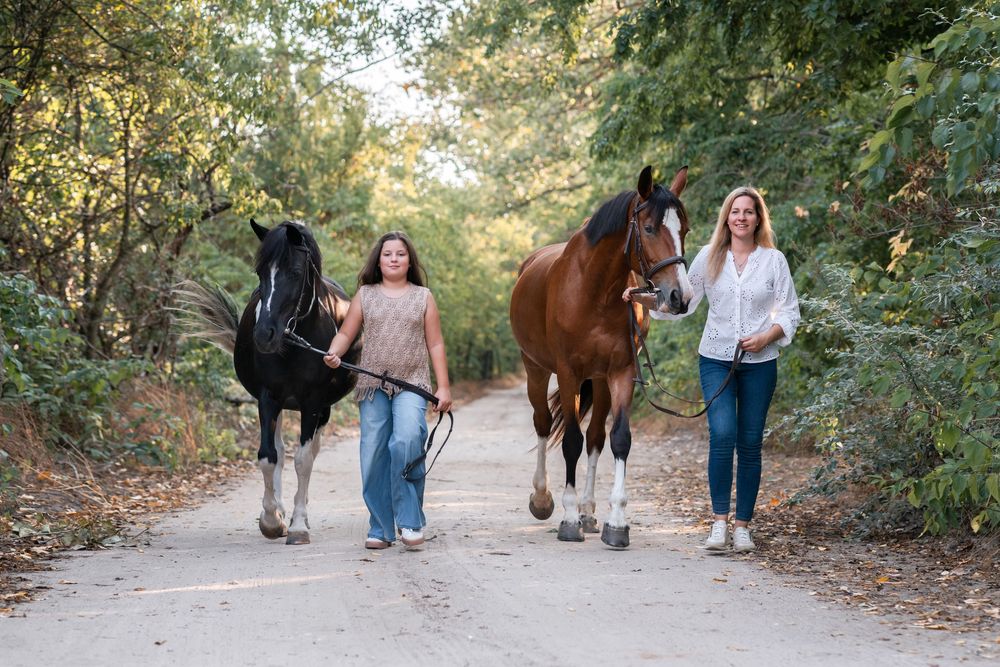 mom and daughter walk horses down a dirt path, one leading a black horse and the other a brown horse family photoshoot in hunter valley