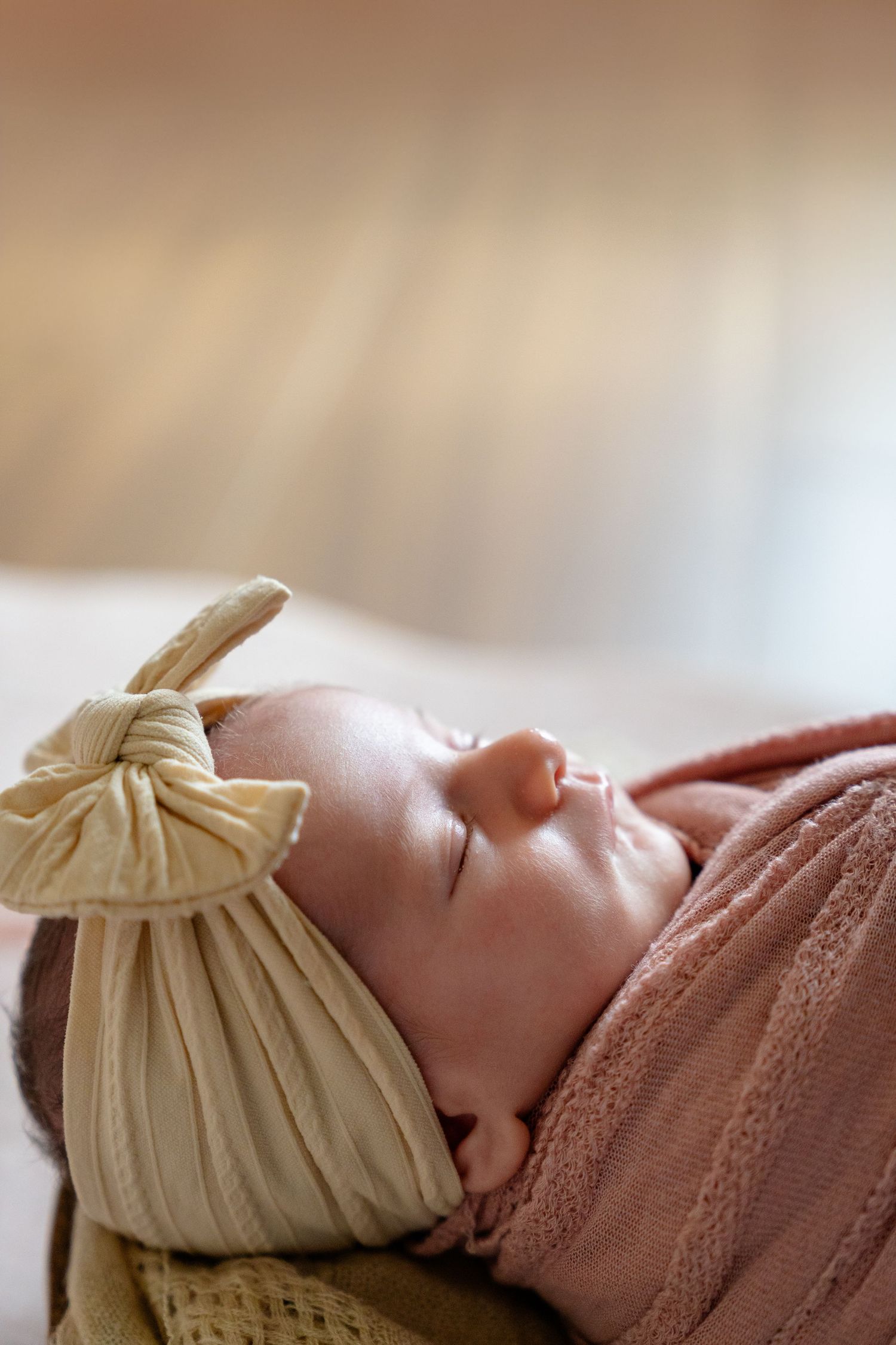 Sleeping newborn baby wrapped in a pink knit blanket wearing a cream ribbed bow headband.