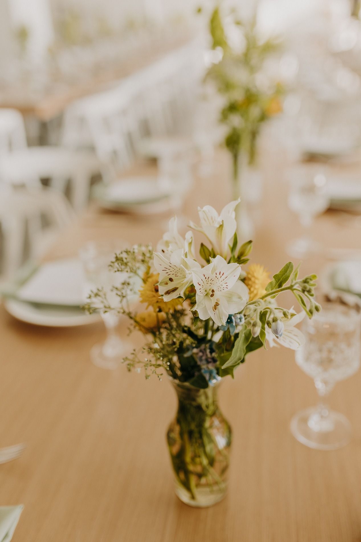 Elegant wedding reception table with crystal glasses, sage green napkins, and yellow floral centerpieces on a wooden table at The Lane.