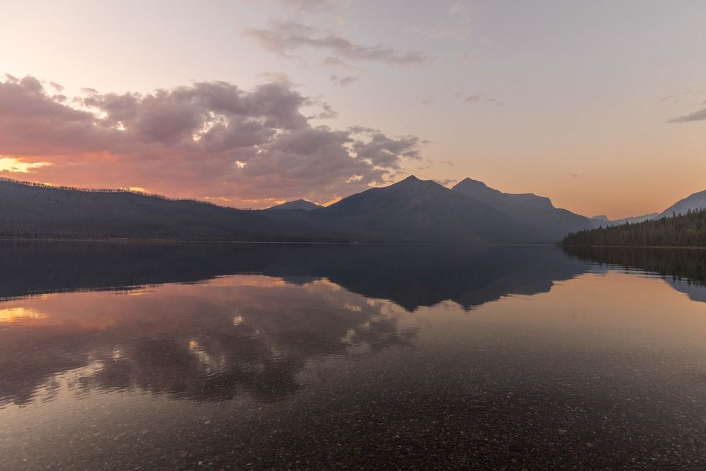 Serene mountain lake at sunset with vibrant pink and orange sky reflecting perfectly on calm glassy water.