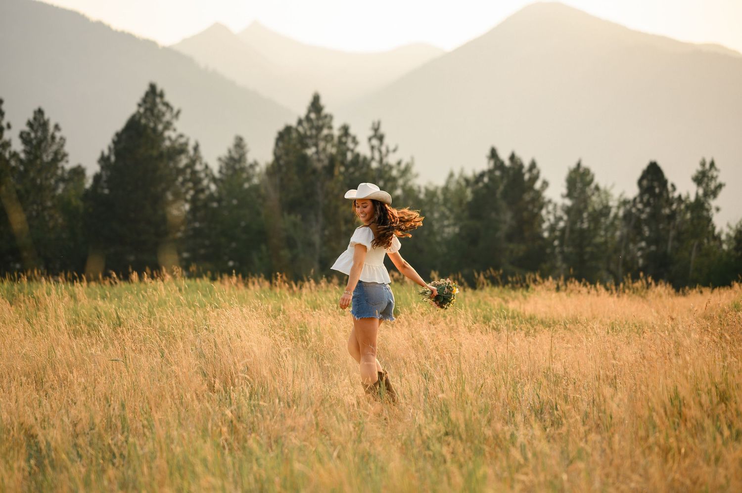 A figure in a white dress poses gracefully in calm lake waters with misty mountains in the background.