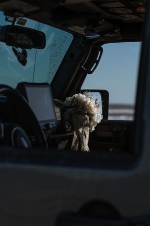 Bridal bouquet of white flowers hanging from Jeep mirror reflecting beach elopement wedding day.