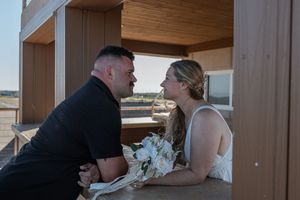 Bride and groom sharing intimate moment seated together at beachside pavilion during golden hour.