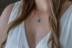 Bride wearing elegant turquoise pendant necklace on silver chain with white V-neck wedding dress.
