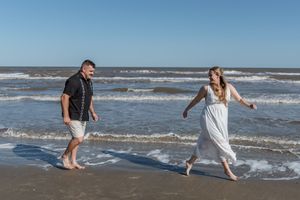 Happy couple walking barefoot along the shoreline on a sunny beach with rolling waves.