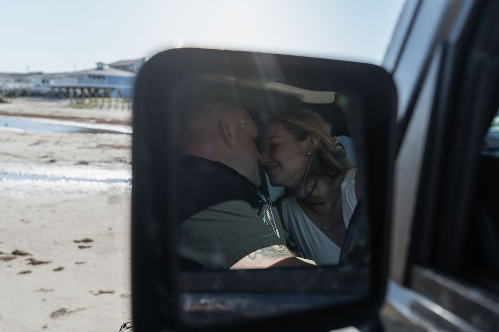 Romantic couple kissing reflected in a vehicle side mirror on a beach setting.
