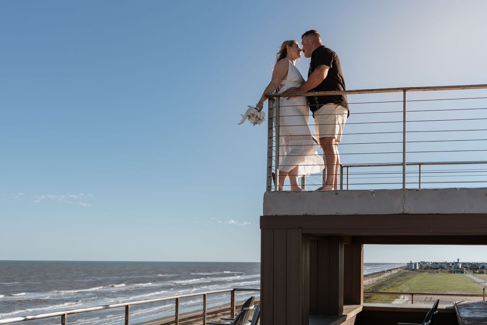 Wedding couple kissing on an elevated oceanfront deck with blue sky and sea views.