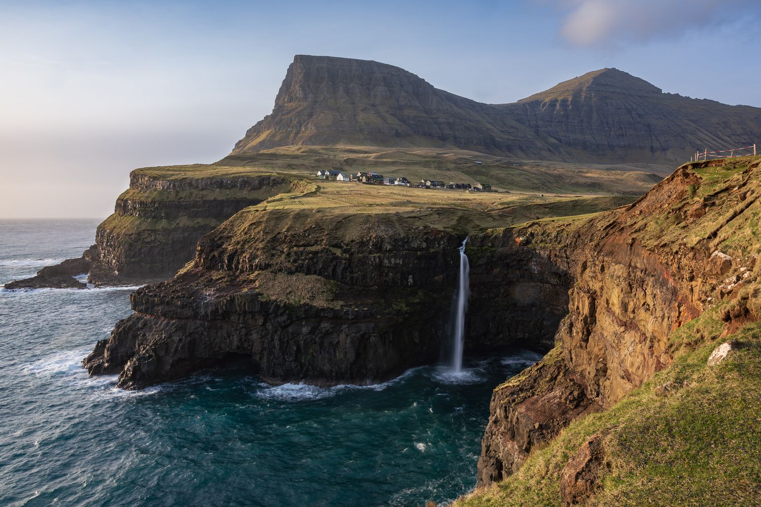 A dramatic waterfall cascades over rugged cliffs into the ocean at Gasadalur, Faroe Islands.
