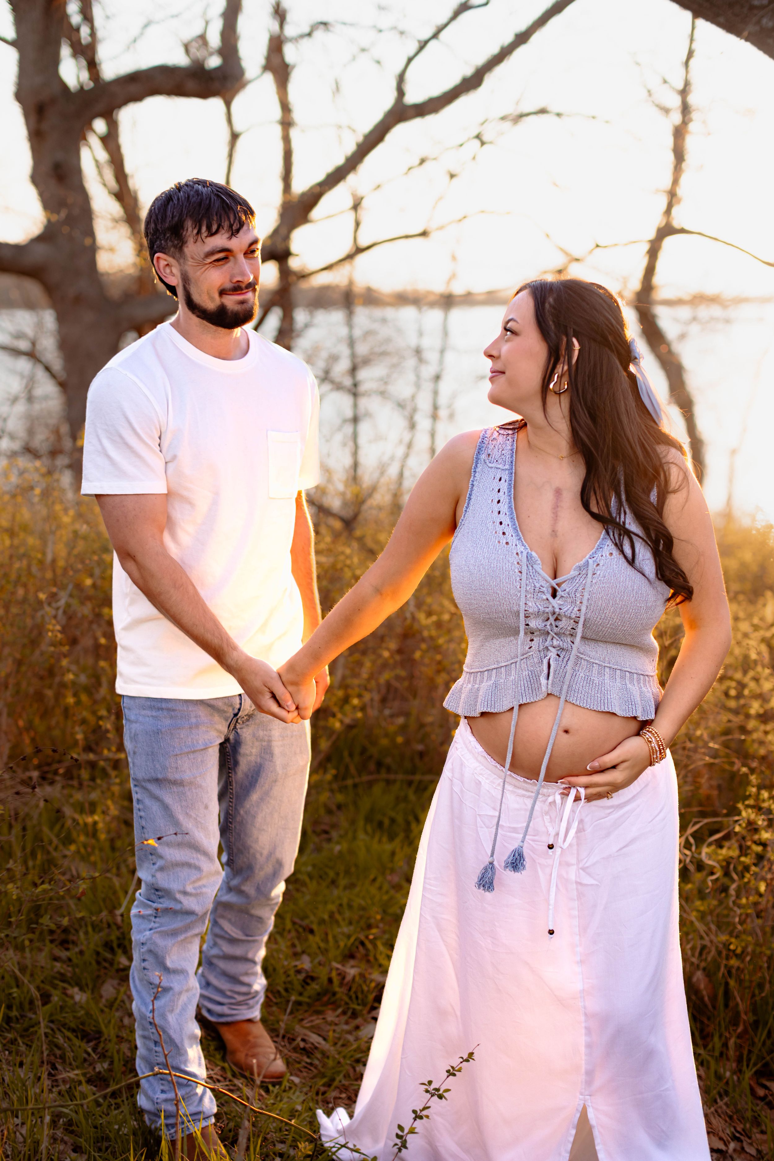 A pregnant woman leads her husband by the hand through a golden field during their Kansas City maternity photo session.