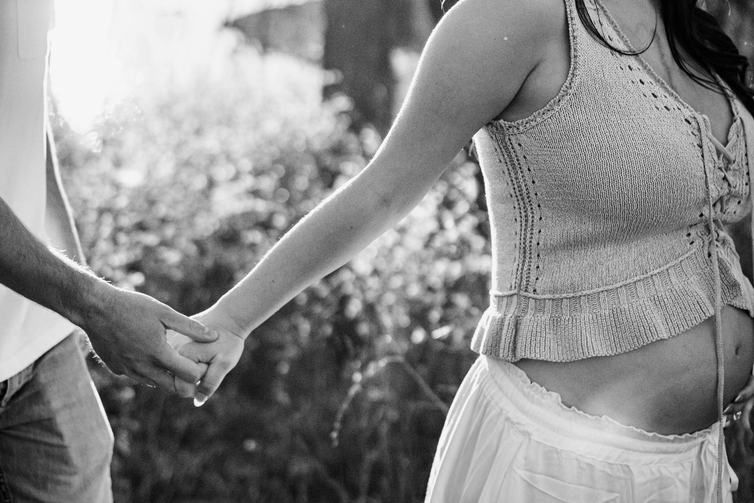 A pregnant woman leads her husband by the hand through a field in a cropped shot from a Kansas City maternity session.